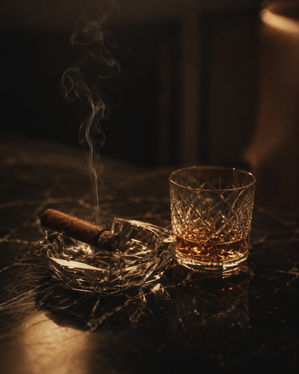 A lit cigar rests on a crystal ashtray beside a cut-glass tumbler of amber spirit on dark marble.